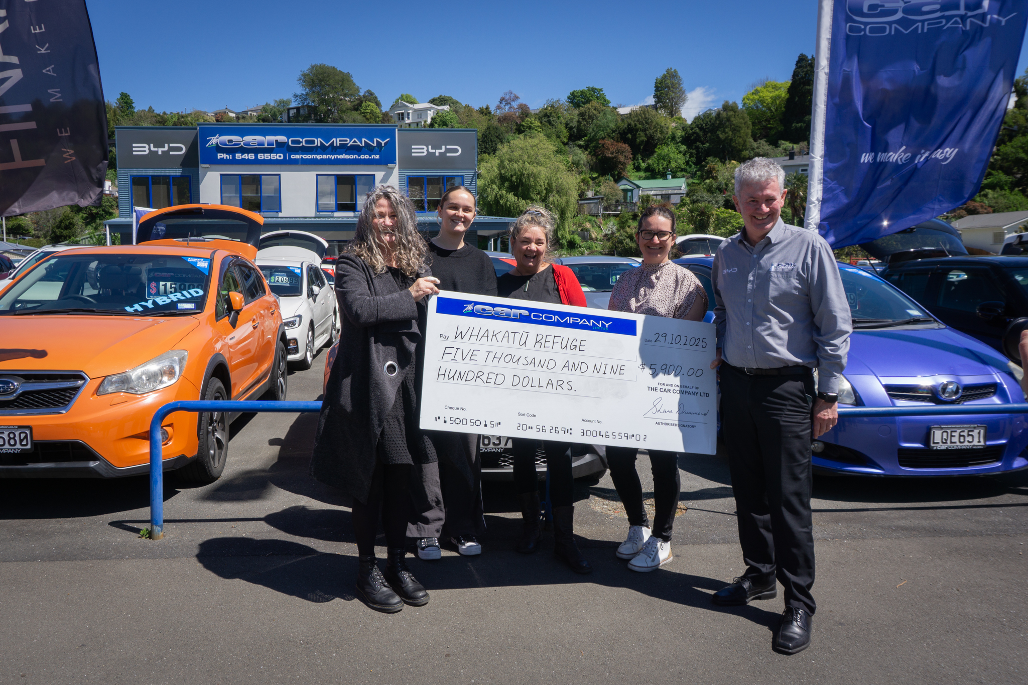 Whakatū Refuge team and SHane Drummond holding donation cheque in front of The Car Company