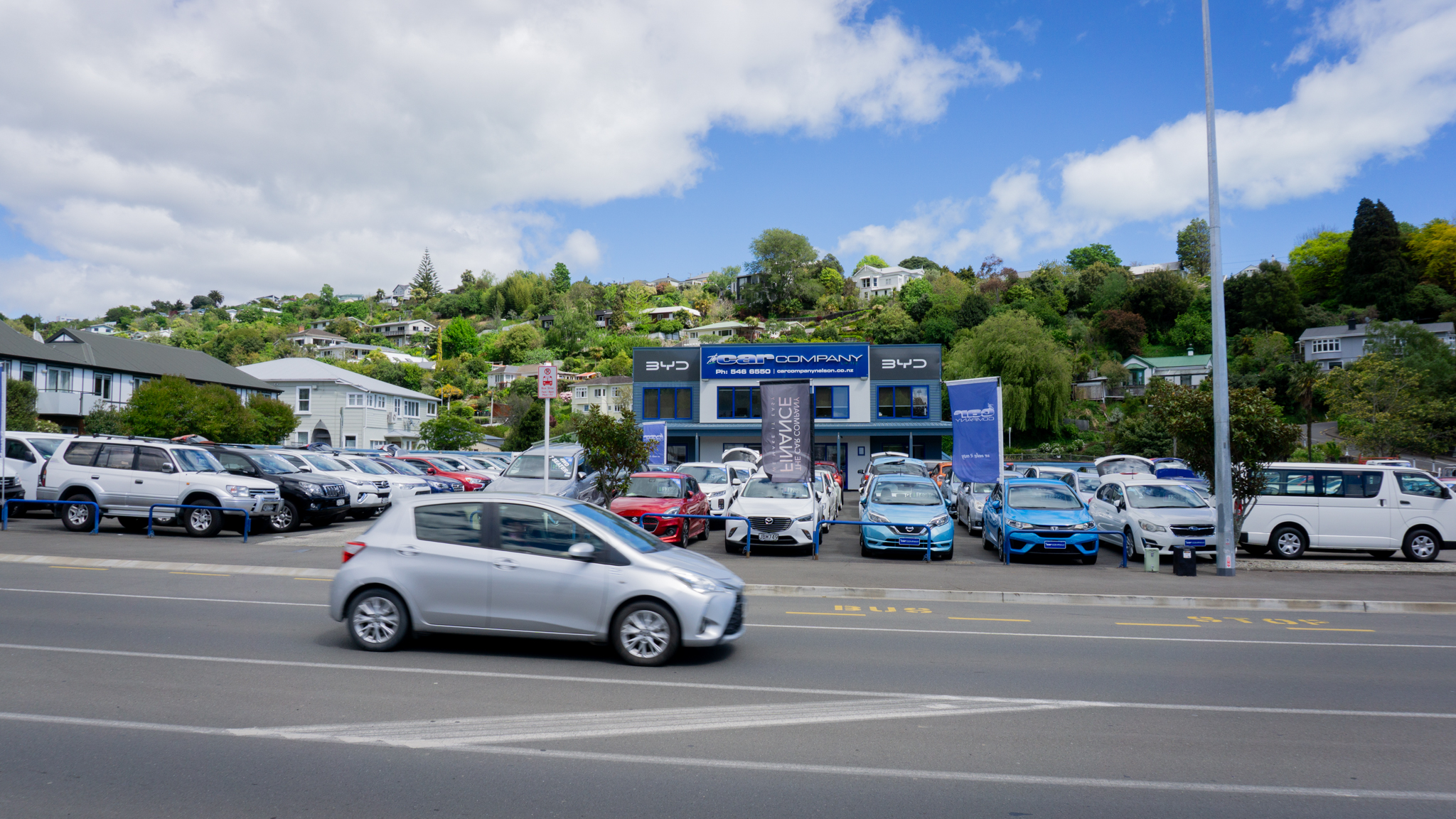 Silver hatch-back car driving past The Car Company Nelson Head Office car yard.