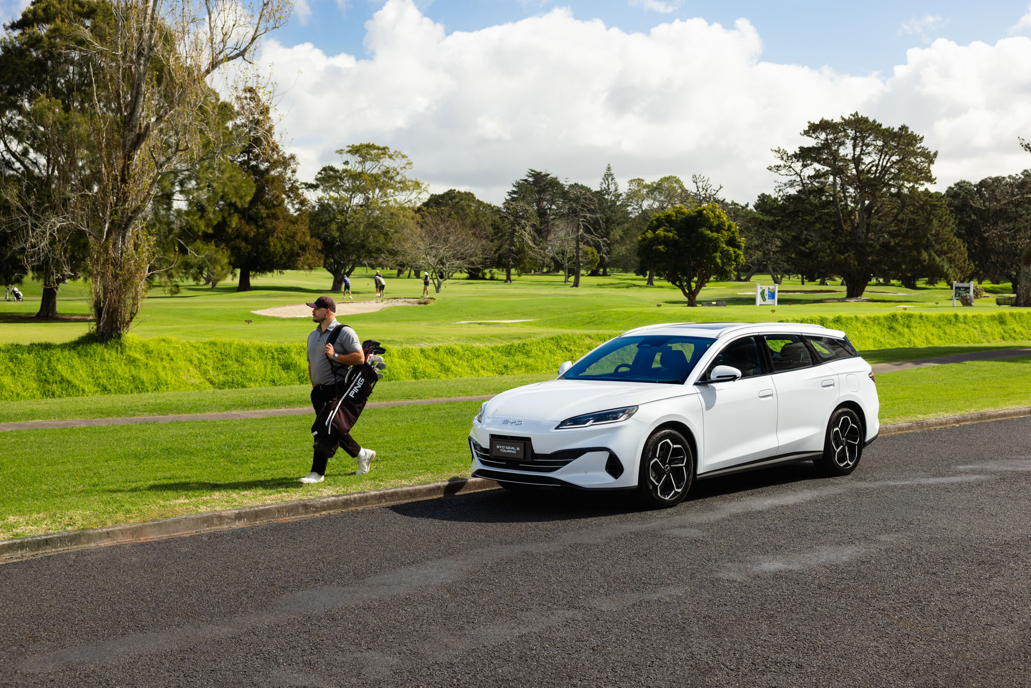 Man carrying golf clubs next to BYD Seal 6 Touring